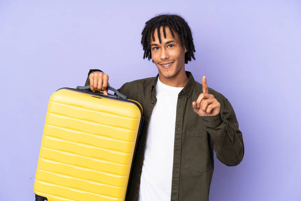 Young african american man isolated on purple background in vacation with travel suitcase and counting one - Photo, Image