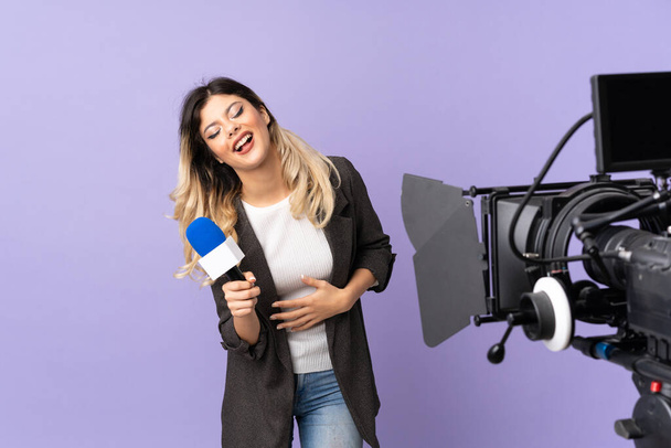 Reporter adolescent fille tenant un microphone et reportage nouvelles isolé sur fond violet souriant beaucoup - Photo, image