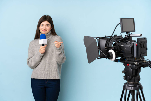 Reportera mujer sosteniendo un micrófono y reportando noticias sobre aislado fondo azul - Foto, Imagen