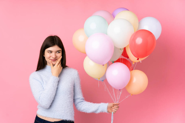 Mladý ukrajinský teenager dívka drží spoustu balónků nad izolované růžové pozadí myšlení nápad - Fotografie, Obrázek