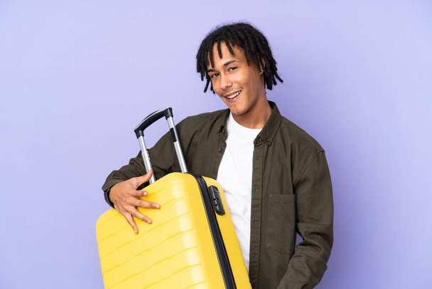 Joven afroamericano aislado sobre fondo púrpura en vacaciones sosteniendo una maleta de viaje como una guitarra - Foto, Imagen