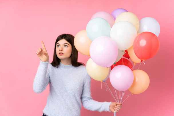 Young Ukrainian teenager girl holding lots of balloons over isolated pink background touching on transparent screen - Valokuva, kuva
