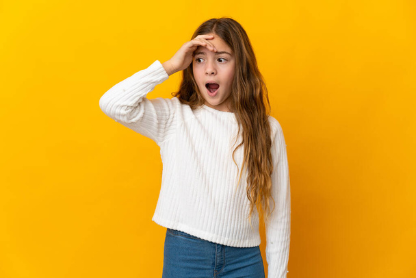 Child over isolated yellow background doing surprise gesture while looking to the side - Photo, Image