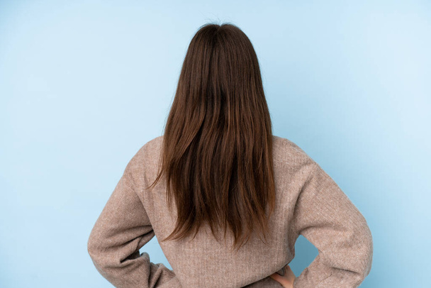 Junge ukrainische Teenager Mädchen trägt einen Pullover über isoliertem blauen Hintergrund in Rückenlage - Foto, Bild