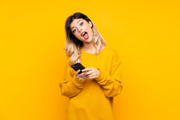 Teenager Mädchen isoliert auf gelbem Hintergrund überrascht und sendet eine Nachricht - Foto, Bild