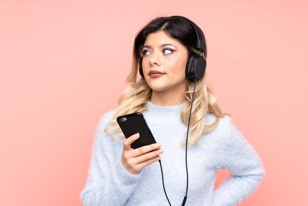 Ragazza adolescente isolata su sfondo rosa ascoltare musica con un cellulare e pensare - Foto, immagini