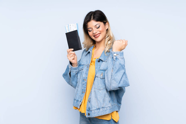 Traveler teenager holding a suitcase isolated on blue background happy in vacation with passport and plane tickets - Foto, Imagem