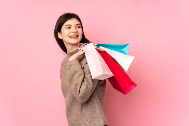 Joven adolescente ucraniano sobre fondo rosa aislado sosteniendo bolsas de compras y sonriendo - Foto, imagen
