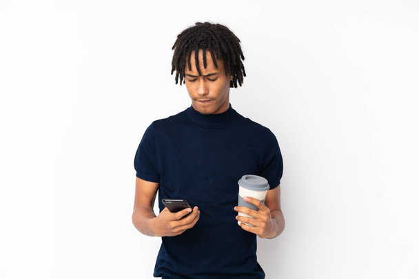 Young african american man isolated on white background holding coffee to take away and a mobile - Foto, Imagem