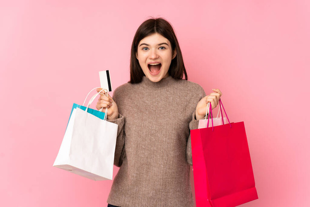 Young Ukrainian teenager girl over isolated pink background holding shopping bags and surprised - Photo, Image