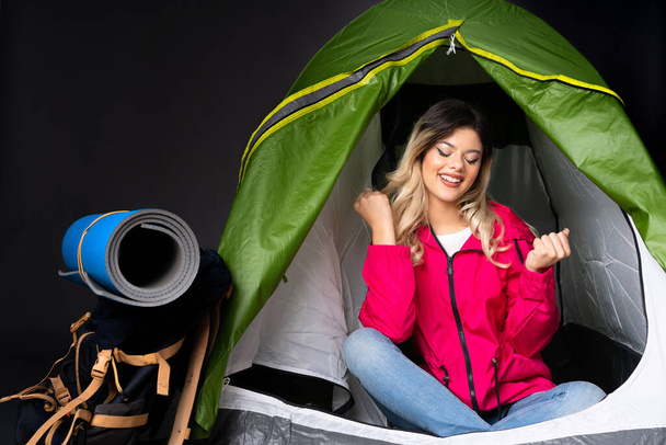 Подросток внутри кемпинга зеленая палатка изолированы на черном фоне с большим пальцем вверх жест и улыбаясь - Фото, изображение