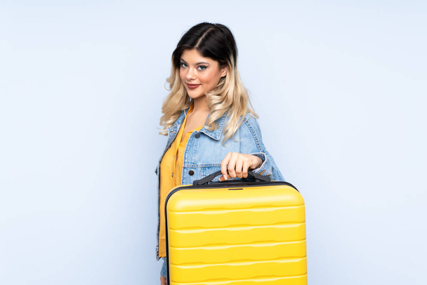 Ταξιδιώτης έφηβος κρατώντας μια βαλίτσα απομονωμένη σε μπλε φόντο στις διακοπές με ταξιδιωτική βαλίτσα και δυστυχισμένος - Φωτογραφία, εικόνα