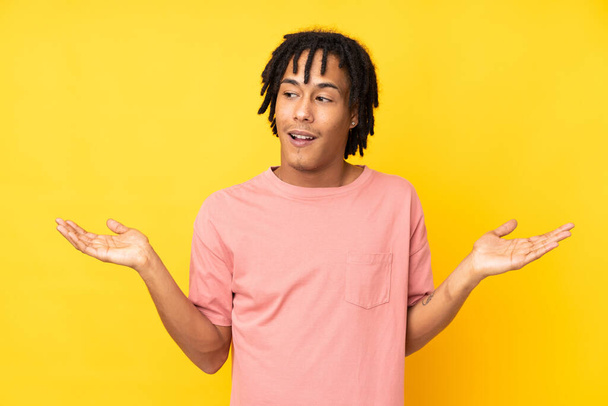Young african american man isolated on yellow background holding copyspace with two hands - Zdjęcie, obraz