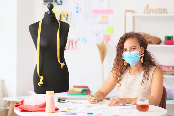 Female fashion designer wearing medical mask in studio - Zdjęcie, obraz