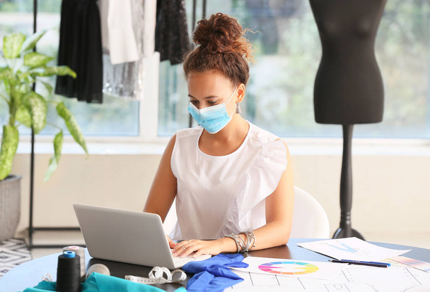 Female fashion designer wearing medical mask in studio - Foto, afbeelding