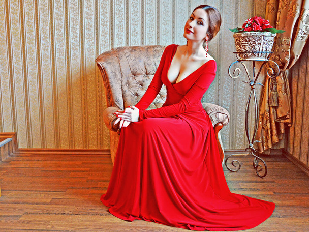 Elegancka kobieta w ciemnych włosach w długiej czerwonej sukience w barokowym, renesansowym lub rokokowym salonie. - Zdjęcie, obraz
