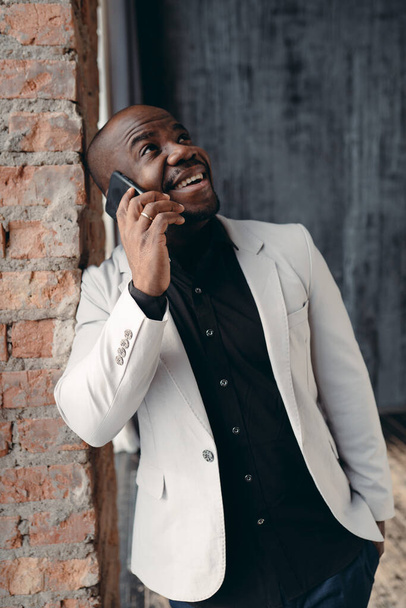 Joyful businessman in a black shirt makes a phone call at work. Online work - Фото, изображение