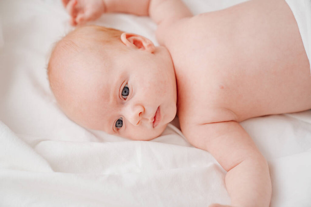 cute red-haired baby lies on a white bed. concept of baby care - Foto, Imagen