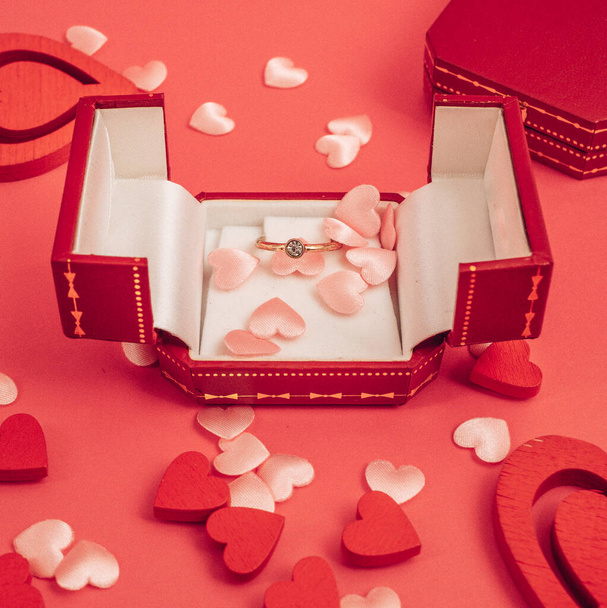 Vista superior sobre la mesa el día de San Valentín, 8 de marzo, Día de las Madres. con una botella de champán, una caja con un anillo, una caja de regalo con un lazo de cinta roja, corazones sobre un fondo rojo - Foto, Imagen