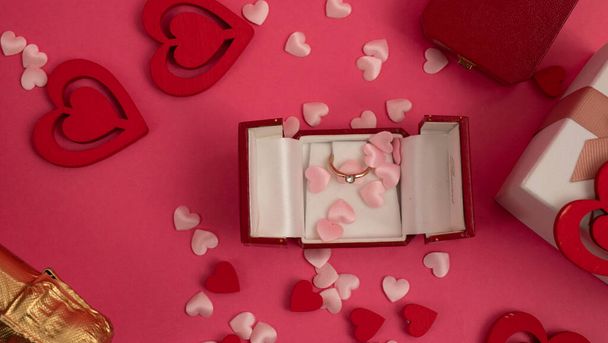 Top zicht op de tafel op Valentijnsdag, 8 maart, Moederdag. met een fles champagne, een doos met een ring, een geschenkdoos met een rode lintstrik, hartjes op een rode achtergrond - Foto, afbeelding