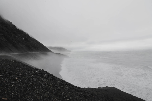 A grayscale shot of cliffs surrounded by the sea covered in the fog - Фото, зображення