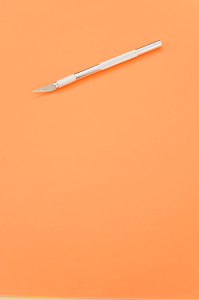 A vertical shot of the metallic scalpel isolated on an orange background - Photo, Image