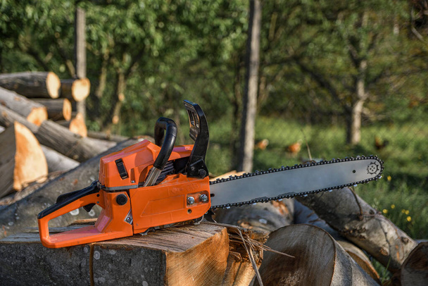 Chainsaw that stands on a heap of firewood in the yard on a background of firewood and trees cut by a chainsaw. - Φωτογραφία, εικόνα