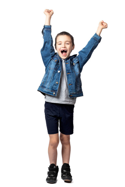 Portrait of a cheerful smiling boy in denim jacket holding fists and rejoicing at his achievements and victory on white isolated background - Foto, Imagem