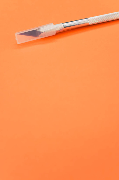 A vertical shot of metallic scalpel with cap isolated on orange background - Fotografie, Obrázek