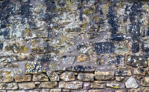 A closeup of a stone fence or stone wall, with different stones and textures. Covered in yellow and white lichen. - Foto, Imagen
