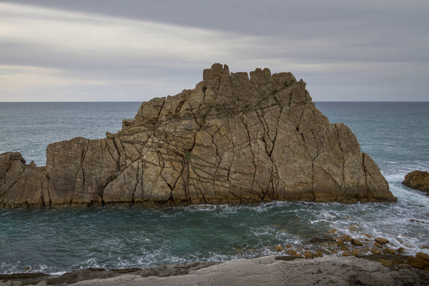 A closeup shot of cliffs in a wavy sea under a cloudy sky - Φωτογραφία, εικόνα
