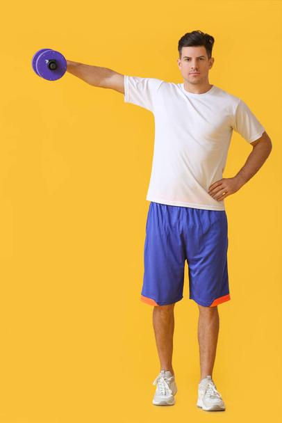 Sporty young man training with dumbbell on color background - Фото, зображення