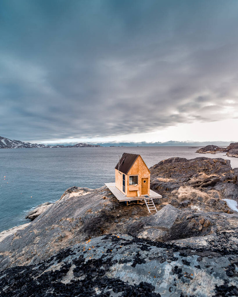 A vertical shot of a small wooden building in a rocky place near the lake under the gloomy sky - Photo, Image