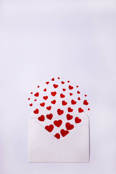 White envelope with red small paper hearts on white background. Valentines Day, love concept. Copy space. Vertical orientation  - Photo, Image