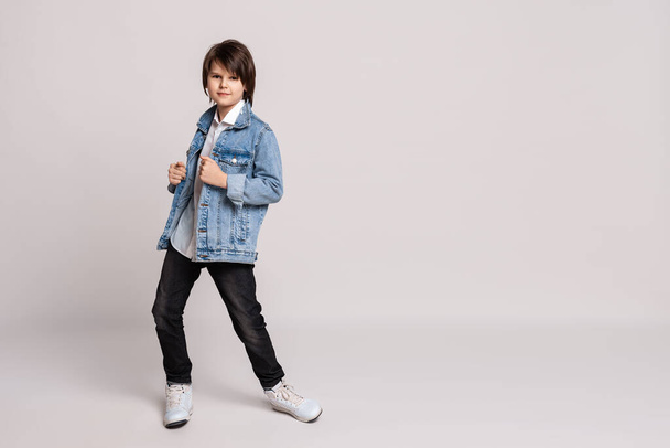 Handsome fashion little boy 11-13 years old in jean jacket posing and dancing in studio. Model Test. Fashion and people concept. Place for ad - Foto, afbeelding