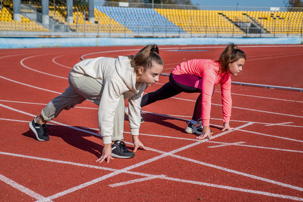 children start on racing track. healthy childhood. workout on fresh air outdoor. confident runner. starting their way. ready set go. teen girls warming up on stadium. kids in sportswear stretching - Photo, image
