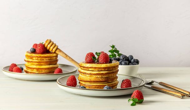 Lekkere Amerikaanse pannenkoeken met frambozen, bosbessen en honing. Familie ontbijt concept met kopieerruimte. - Foto, afbeelding