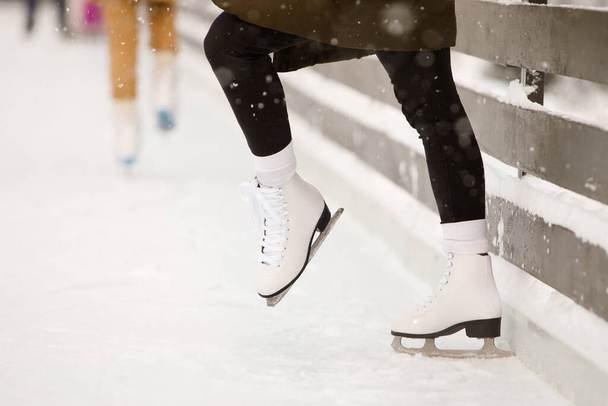 Primer plano de las piernas del patinador mujer en pista de patinaje abierta, vista lateral. Patines blancos femeninos sobre hielo, trenes cerca de la pared, aprendiendo a equilibrarse. Actividades de fin de semana al aire libre en clima frío.  - Foto, Imagen