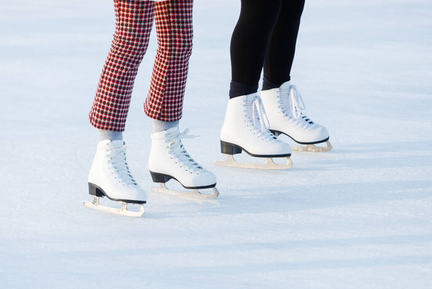 Nahaufnahme der Beine von Frauen auf Schlittschuhen im Winter auf einer offenen Eisbahn. Die Schlittschuhe zweier Freunde beim gemeinsamen Schlittschuhlaufen an einem Winternachmittag. Winterzeit, Outdoor-Aktivitätskonzept - Foto, Bild