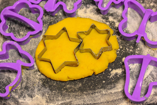 Formy w kształcie gwiazdy i świeżo ugniatane żółte ciasto wewnątrz, czarna deska do krojenia posypana białą mąką. Domowe zdrowe wypieki  - Zdjęcie, obraz