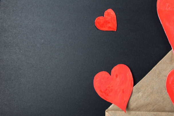 Red hearts drop out of crafting brown envelope on black background with a copy of the space. - Photo, Image