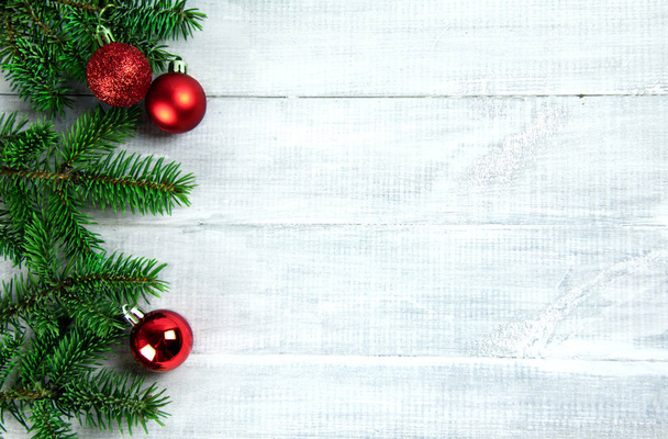 Σπρους κλαδιά βρίσκονται σε μια λευκή ξύλινη σανίδα στην αριστερή πλευρά με κόκκινα χριστουγεννιάτικα στολίδια - Φωτογραφία, εικόνα