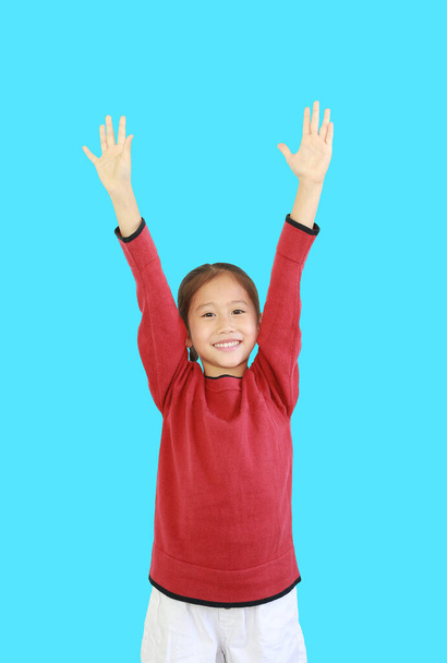Cheerful asian little kid girl in red long sleeve shirt holding hands up isolated on cyan background. Student question and answer concept - Fotó, kép