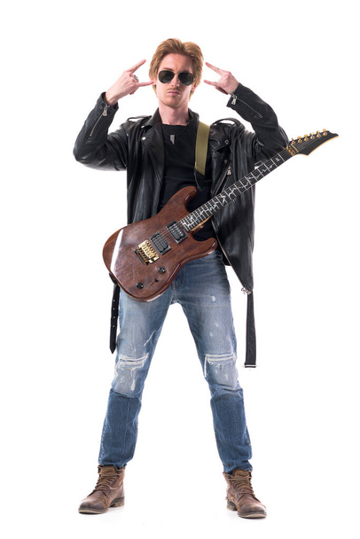 Cool macho elegante musicista rock con chitarra elettrica che mostra il segno della mano del corno dell'hard rock. Corpo intero isolato su sfondo bianco.  - Foto, immagini