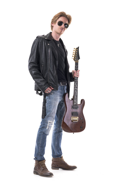 Крутий асертивний гітарист, що стоїть з електрогітарою в стильному рокерному одязі. Повне тіло ізольоване на білому тлі
.  - Фото, зображення