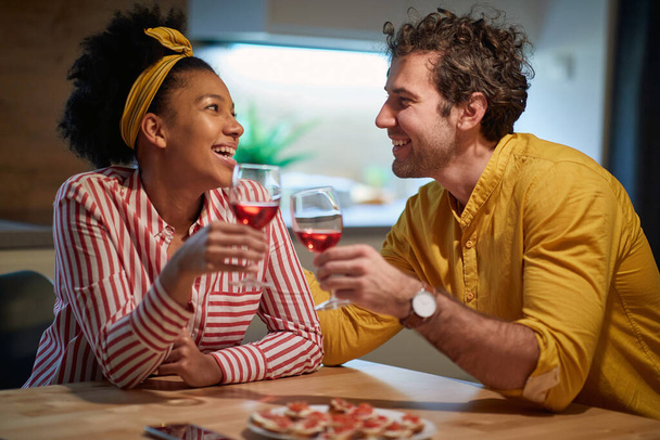 Happy mixed couple relaxing and drinking wine together at home - Foto, imagen