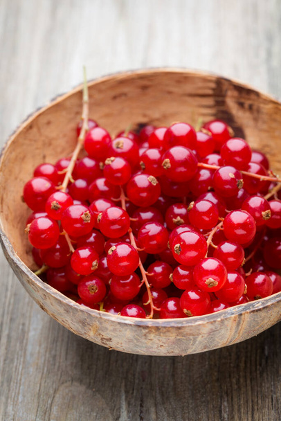 Redcurrant on a branch close to a wooden bowl. - Foto, afbeelding