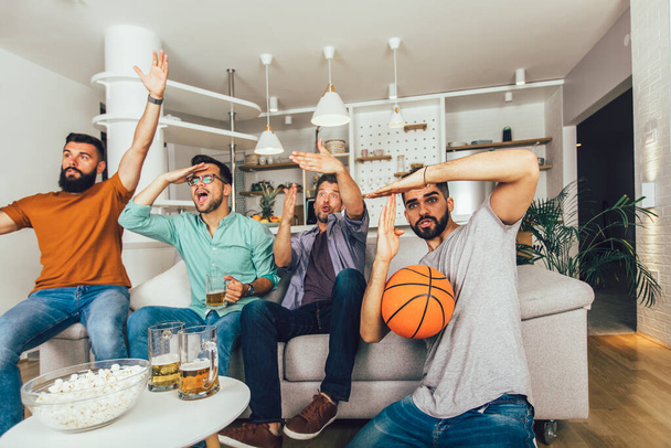 Ευτυχισμένοι φίλοι ή οπαδοί του μπάσκετ βλέποντας μπάσκετ στην τηλεόραση και γιορτάζοντας τη νίκη στο σπίτι. - Φωτογραφία, εικόνα