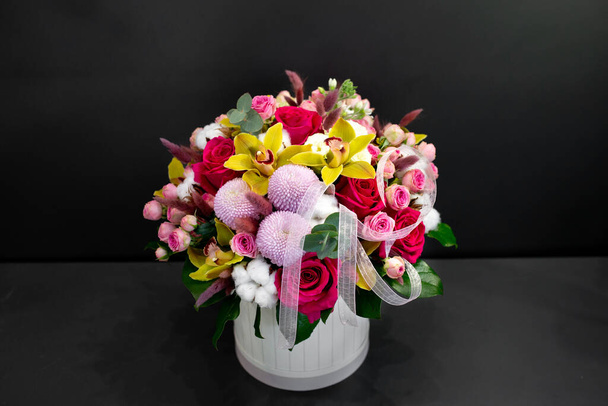 Floral arrangement with orchids, cotton and other flowers in a large hat box on a dark background. - Фото, изображение