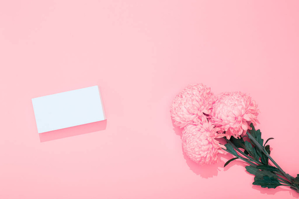 Ramo de exuberantes crisantemos y caja de regalo blanca sobre fondo rosa con espacio para copiar. Vacaciones o tarjeta de visita. Feliz cumpleaños, San Valentín 14 de febrero, Día de la Mujer 8 de marzo, Día de la Madre 8 de mayo. Burla. - Foto, Imagen